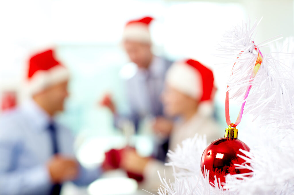 People celebrating in office, the focus is on glass ball on Christmas tree