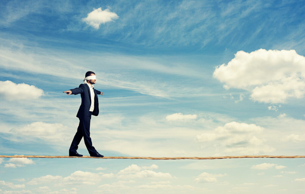 man with the blindfold walking on the rope over blue sky